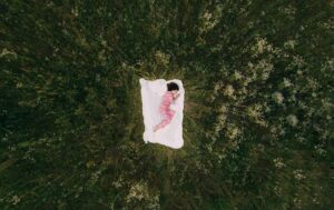 A peaceful aerial view of a person in pajamas sleeping on a blanket in a grassy field.